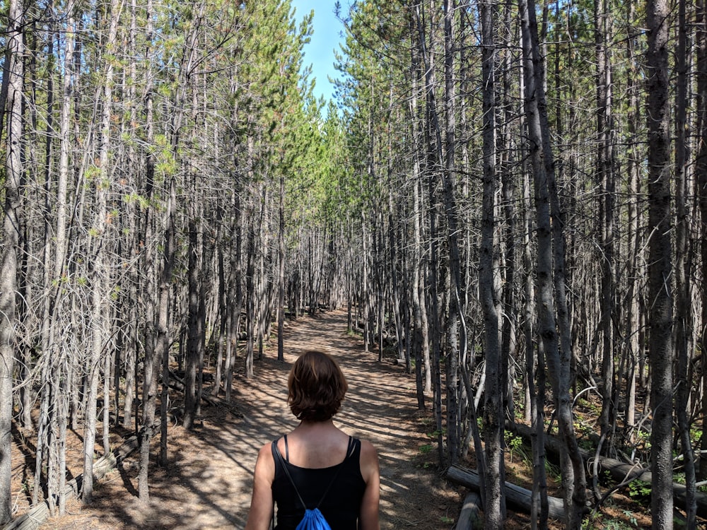 woman in blue tank top standing in the middle of forest during daytime