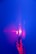 A hand holds a transparent object, illuminated by a vibrant pink and purple light against a deep blue background. The word 'PRISM' is projected repetitively on the hand and object, creating a dynamic play of light and shadow.