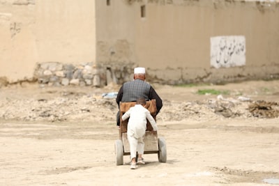 man in white long sleeve shirt and white pants sitting on brown sand during daytime afghanistan zoom background