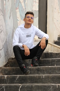 man in white long sleeve shirt and black pants sitting on concrete stairs
