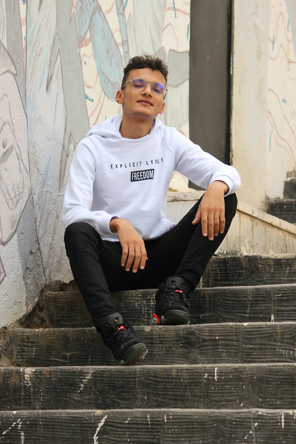 man in white long sleeve shirt and black pants sitting on concrete stairs