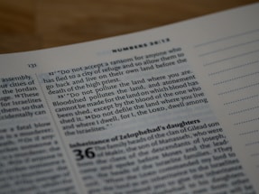 A close-up of an open book, focusing on printed text with a verse from Numbers 35:33. The page is well-lit with a clear serif font, and there are dotted lines on the right margin.