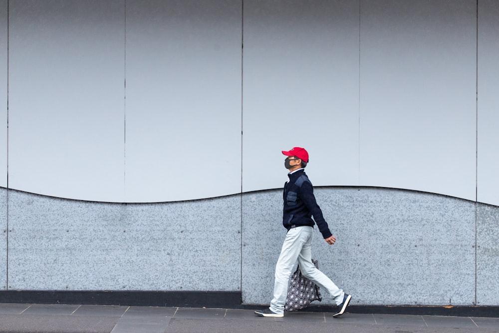 man in black jacket and gray pants wearing red cap walking on gray concrete floor