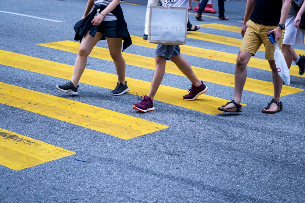 昼間、灰色のアスファルト道路に立つ黒いミニドレスと黄色い靴の女性