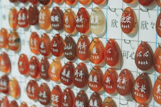 A grid display featuring multiple orange and red teardrop-shaped stones with white Chinese characters engraved on them, each hanging from a hook against a white background with more characters.