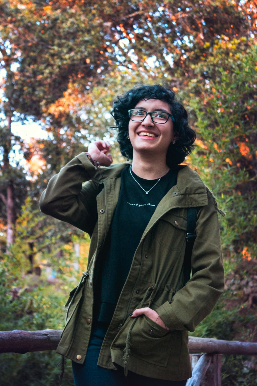 woman in green jacket standing near brown and green leaf trees during daytime