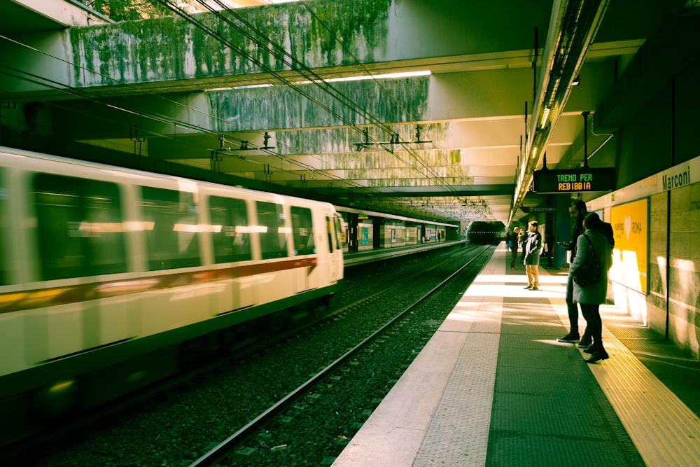 people walking on sidewalk near white and green train during night time