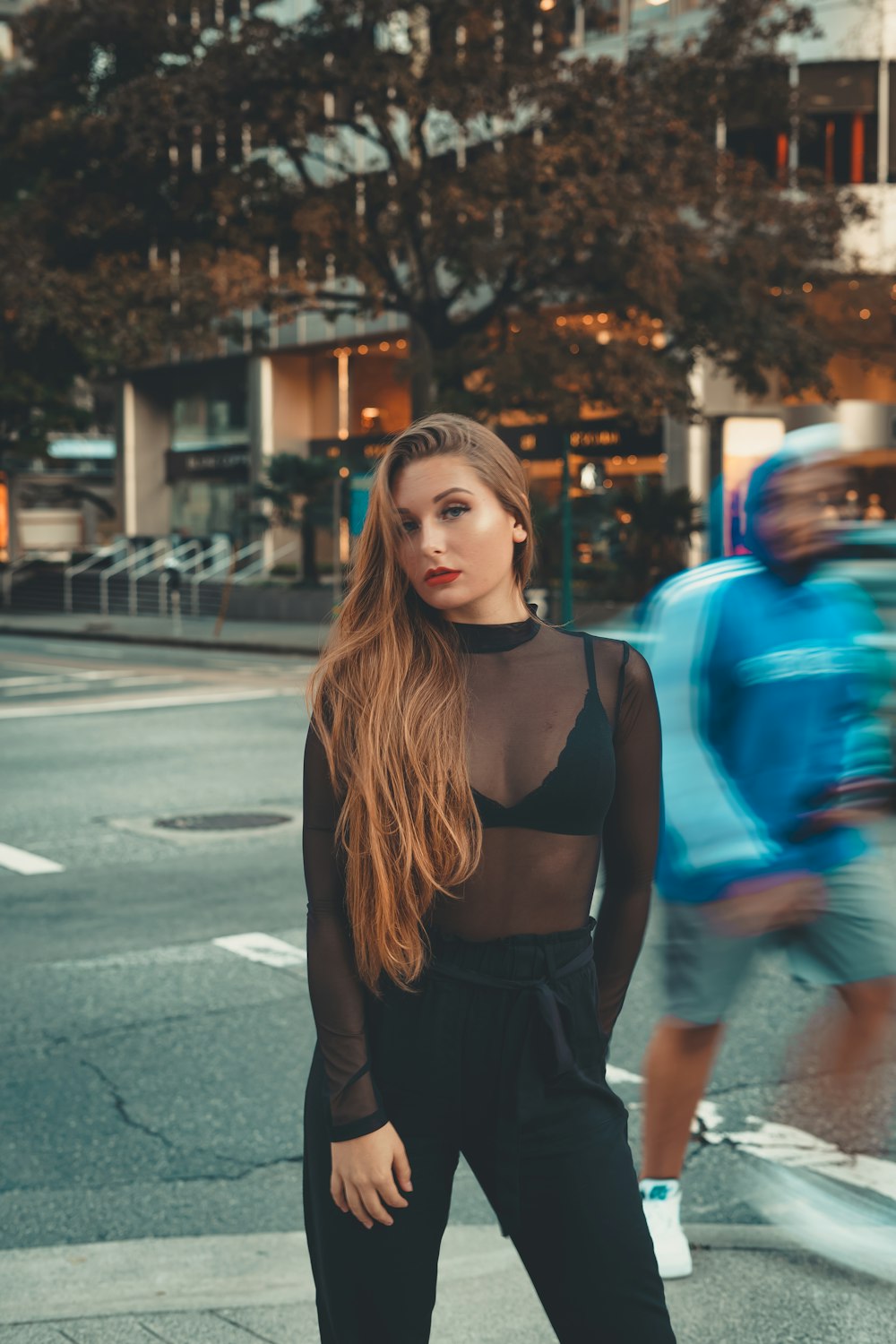 woman in black tank top and blue denim jeans standing on sidewalk during daytime