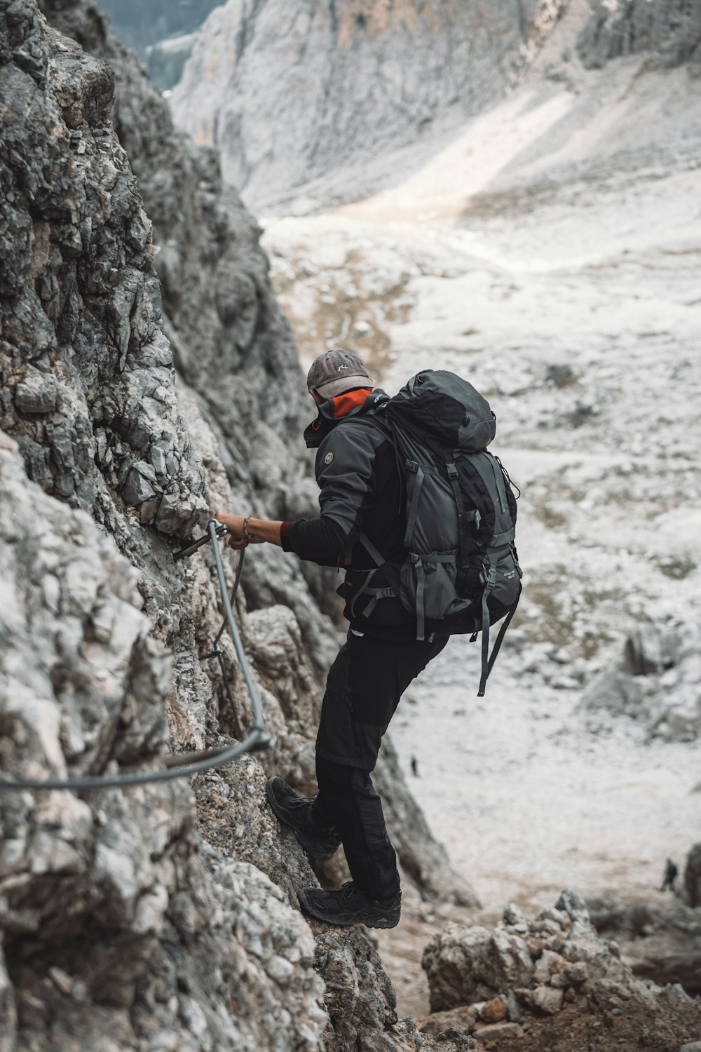 man in black jacket and black pants with black backpack climbing on brown rock mountain during