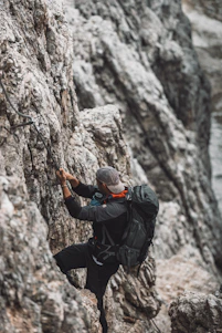 A person wearing high-tech clothing climbing a rugged mountain trail at sunrise.