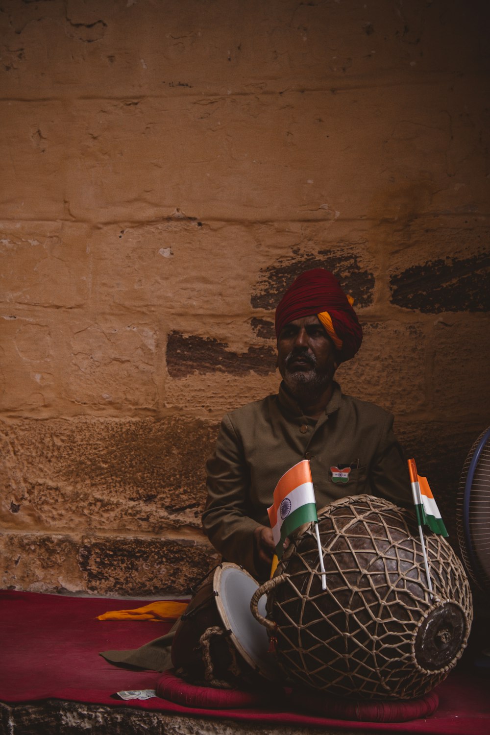 man in black jacket and red knit cap sitting on brown concrete floor