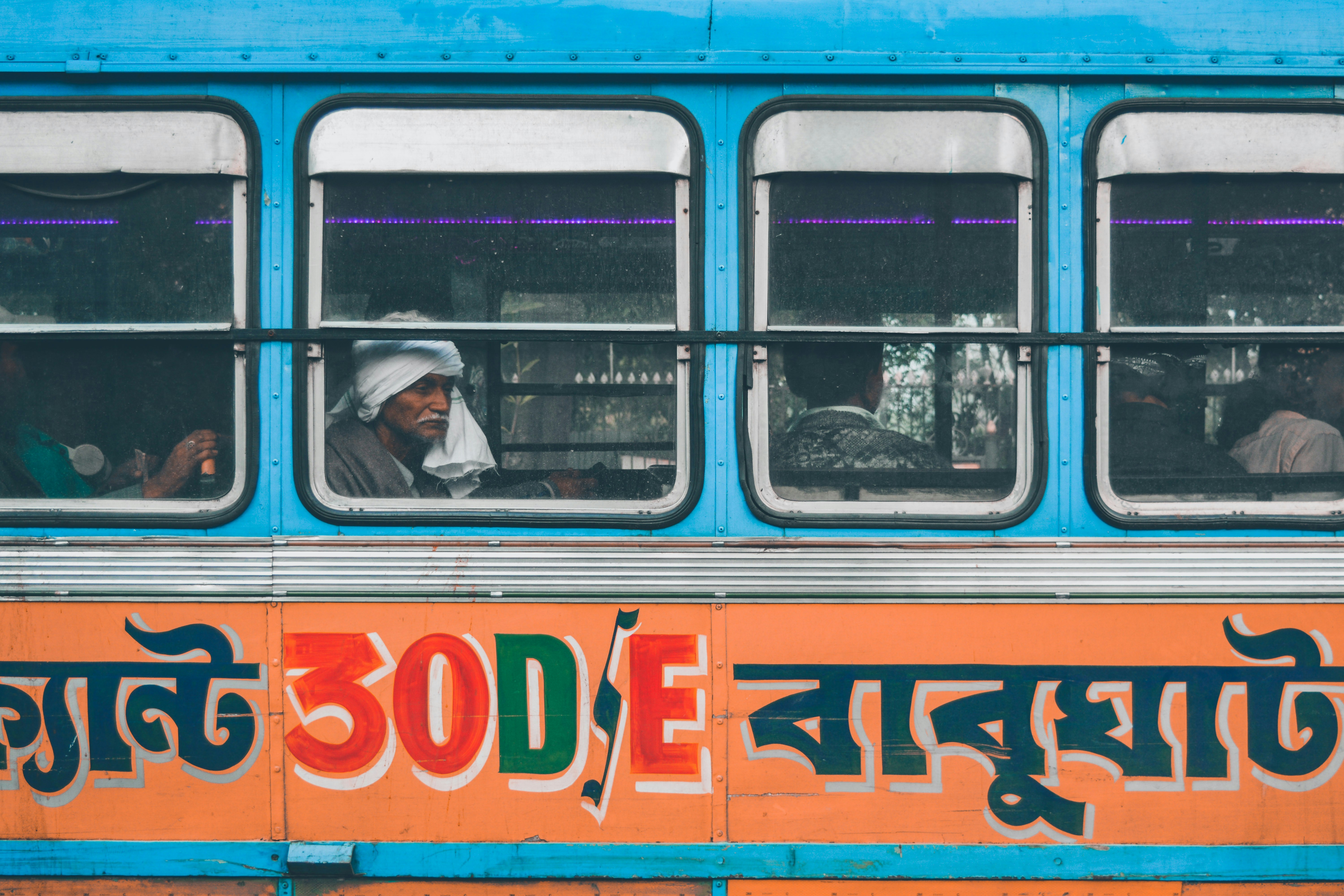 man in black jacket and blue denim jeans sitting on blue and orange bus
