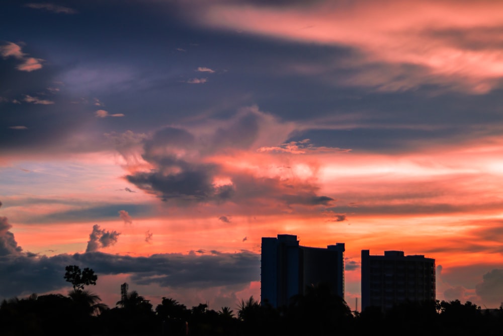 a sunset with clouds and buildings in the background