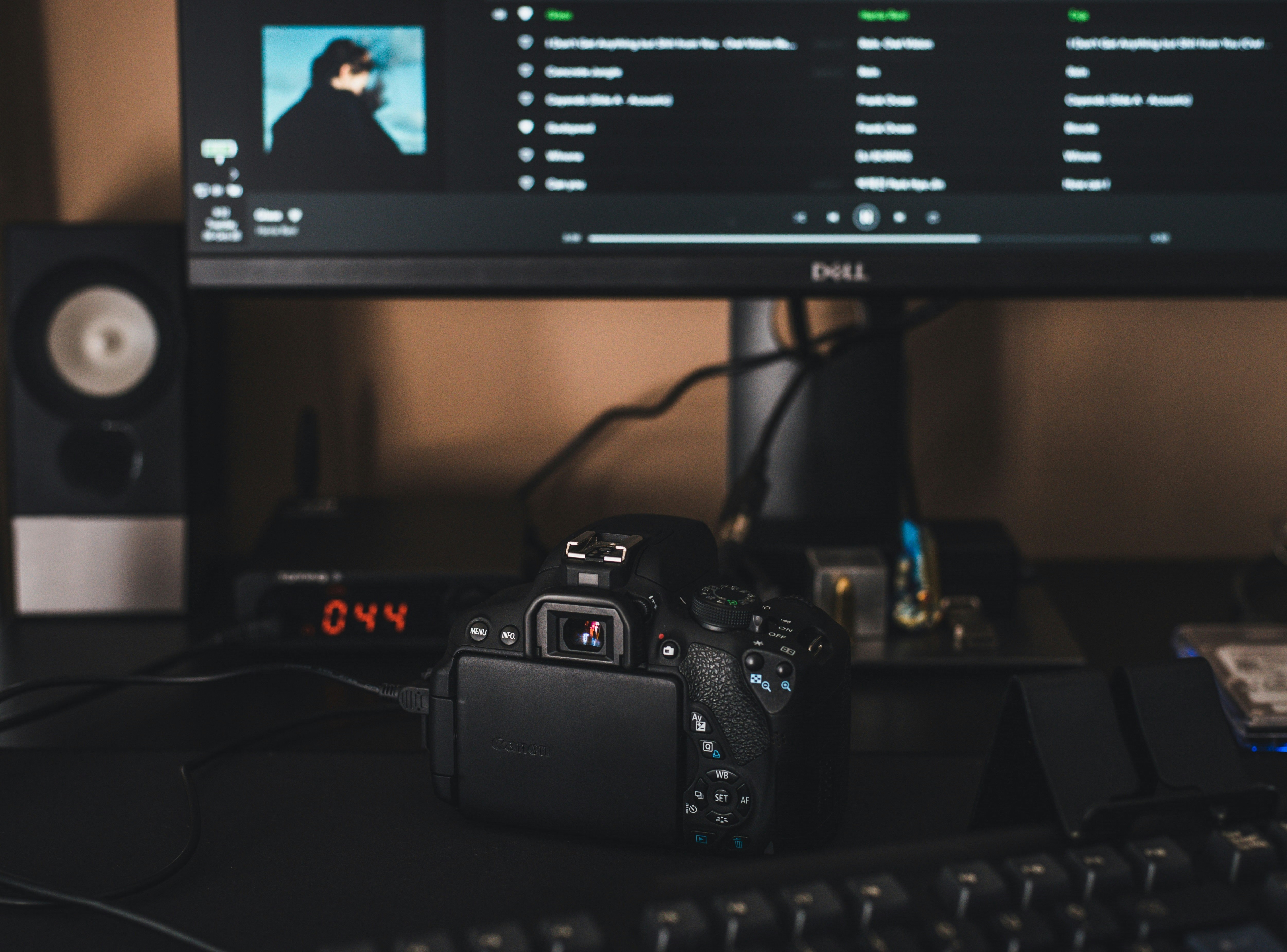 A DSLR video camera sits next to a computer, which is uploading video. Asking, “how do royalties work on Spotify?” caused the video editor to choose royalty free music from Soundstripe for his video instead.