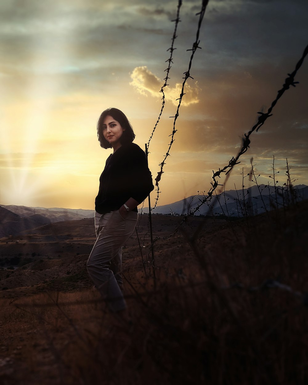 woman in black long sleeve shirt and gray pants standing on brown field during sunset