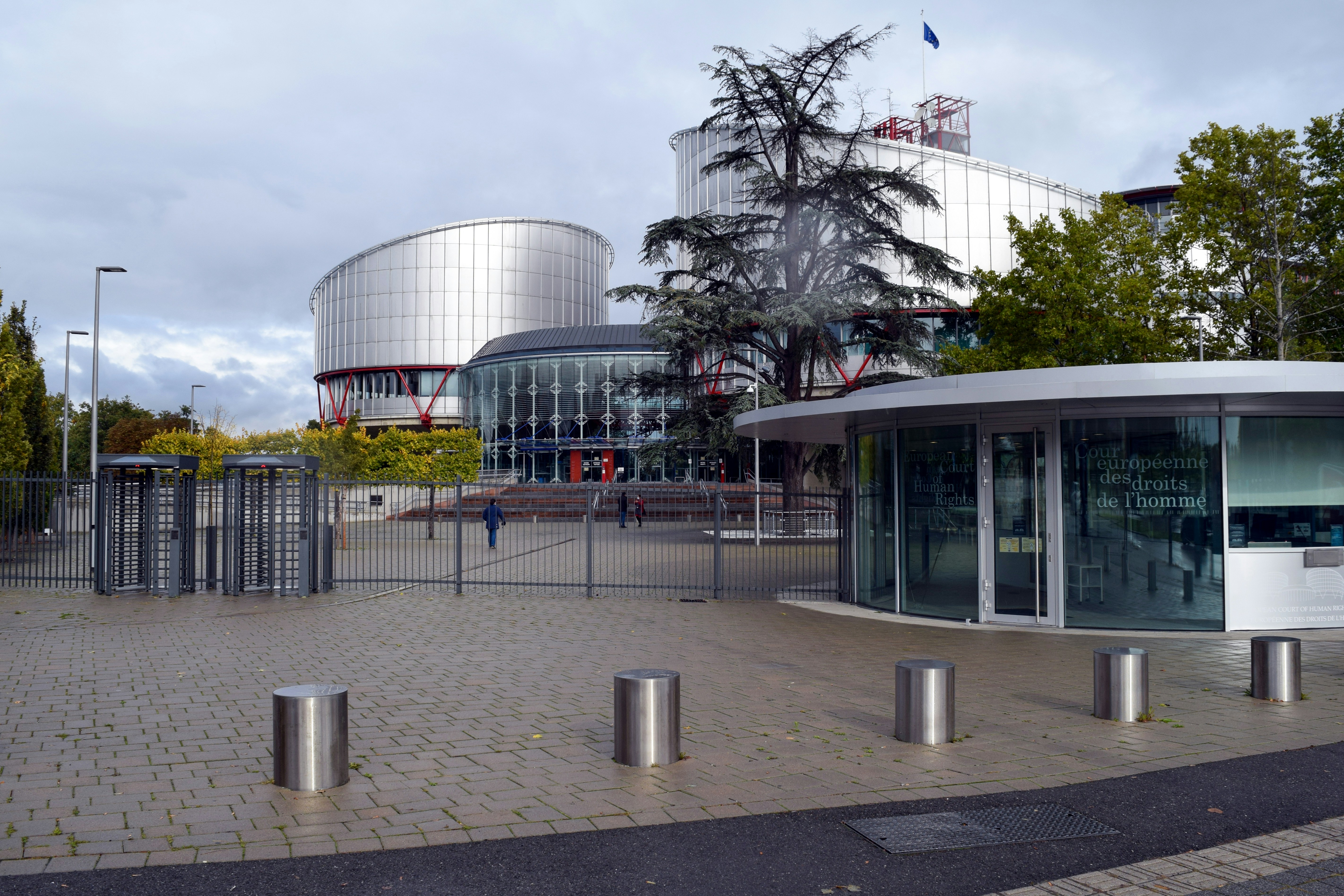 Modern glass and metal building of the European Court of Human Rights in Strasbourg, behind a secure gated entrance.