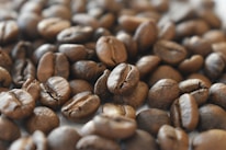 A close-up of coffee beans scattered on a textured surface, highlighting their rich color and texture.