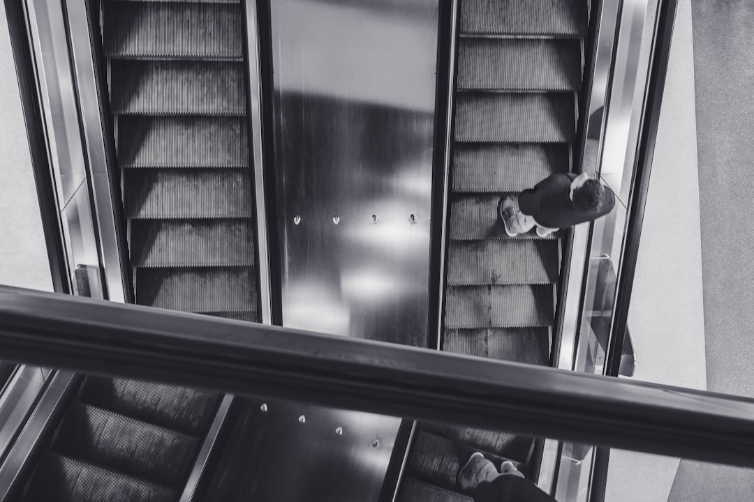 grayscale photo of man in black jacket and pants sitting on stairs