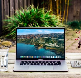 macbook pro beside clear drinking glass on brown wooden table