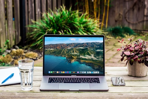 macbook pro beside clear drinking glass on brown wooden table