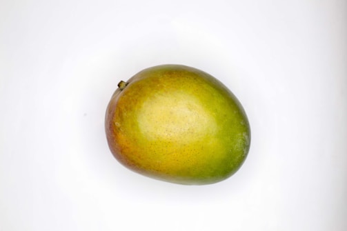 A ripe mango with a gradient coloration from green to yellow and shades of red is placed on a plain white background.