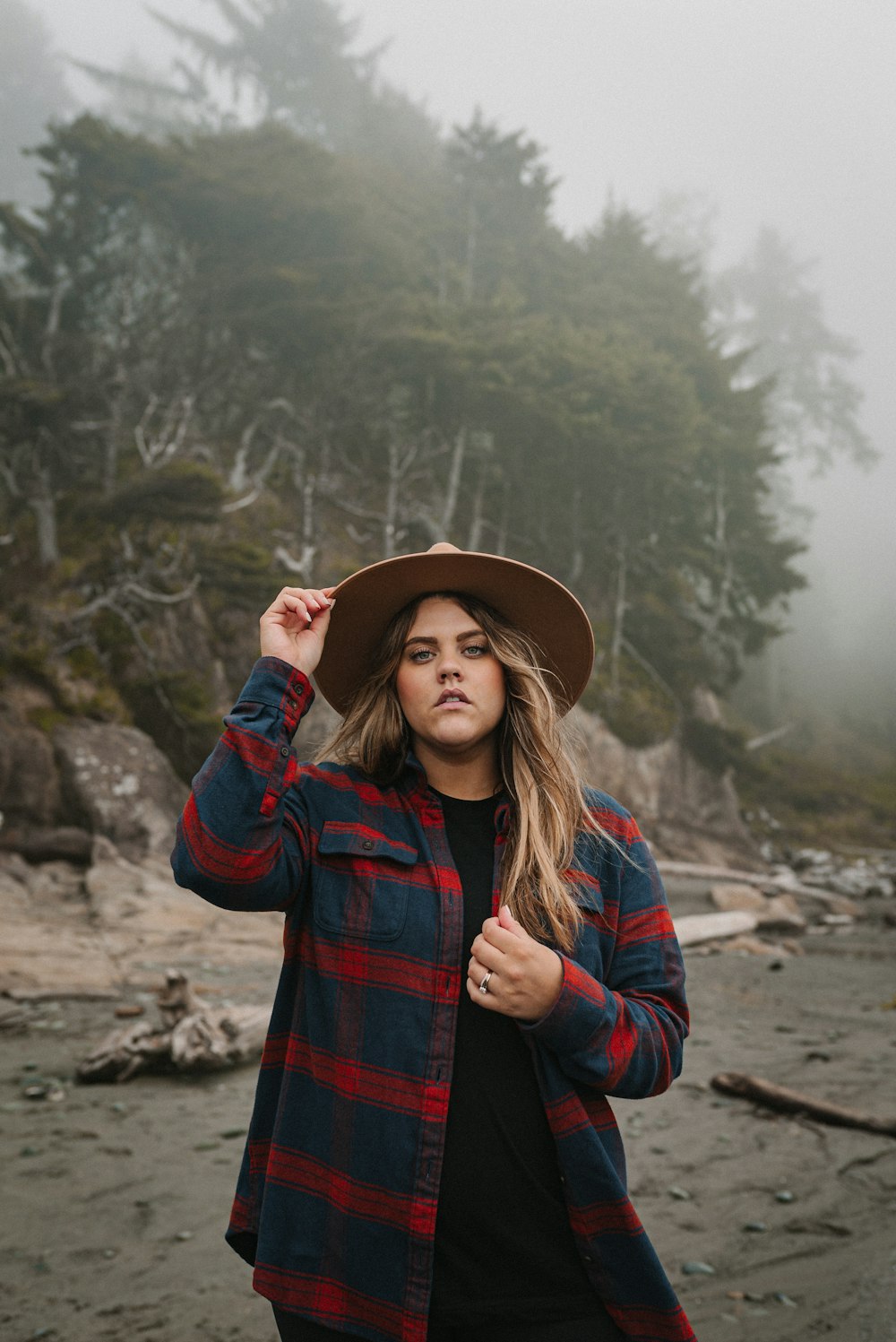 Femme en manteau à carreaux rouge et noir portant un chapeau marron debout sur le sable brun pendant la journée