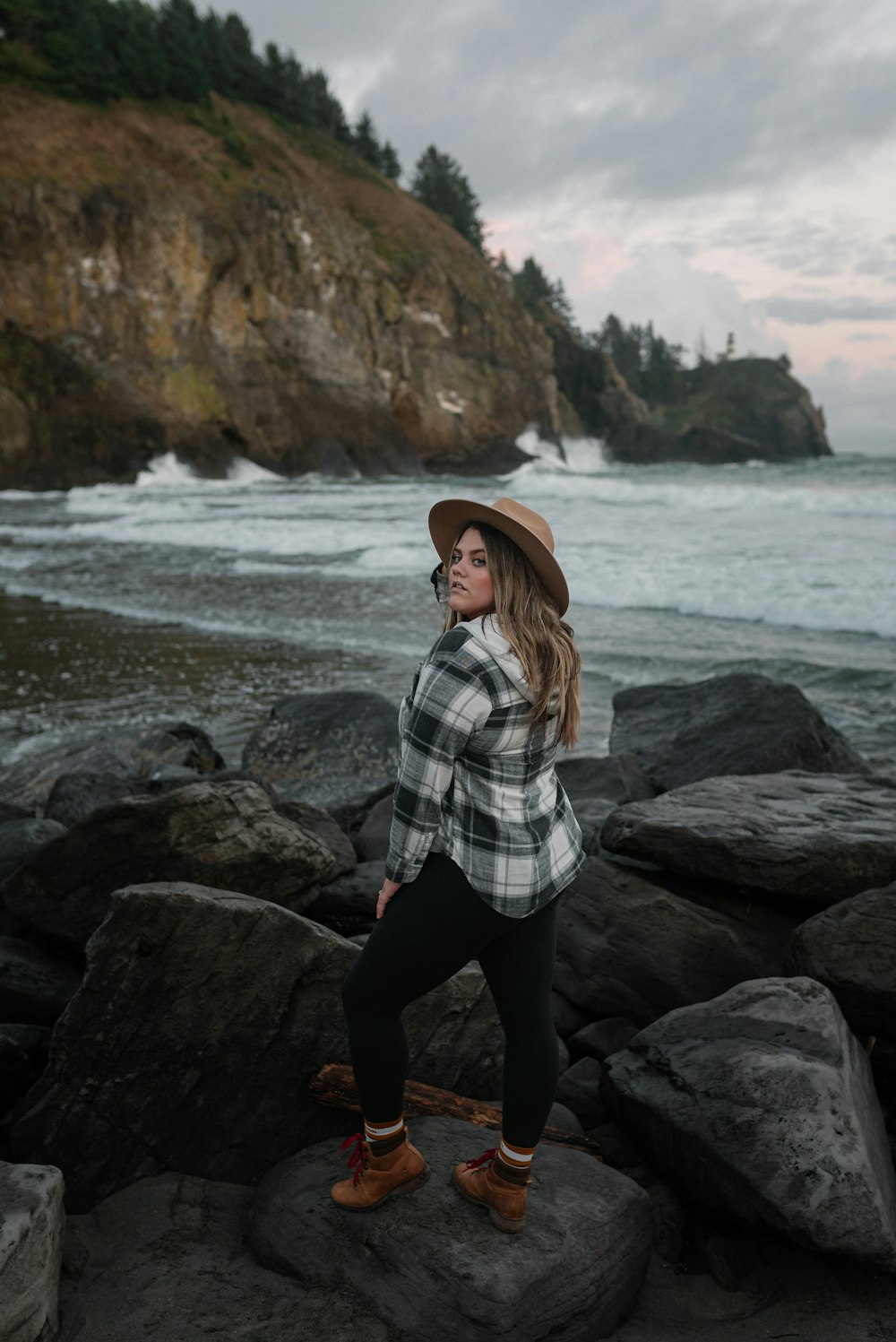 woman in white and black plaid dress shirt and black pants sitting on rock near sea