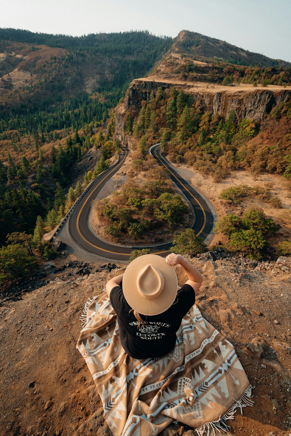 person in black and white long sleeve shirt and beige cowboy hat sitting on brown rock