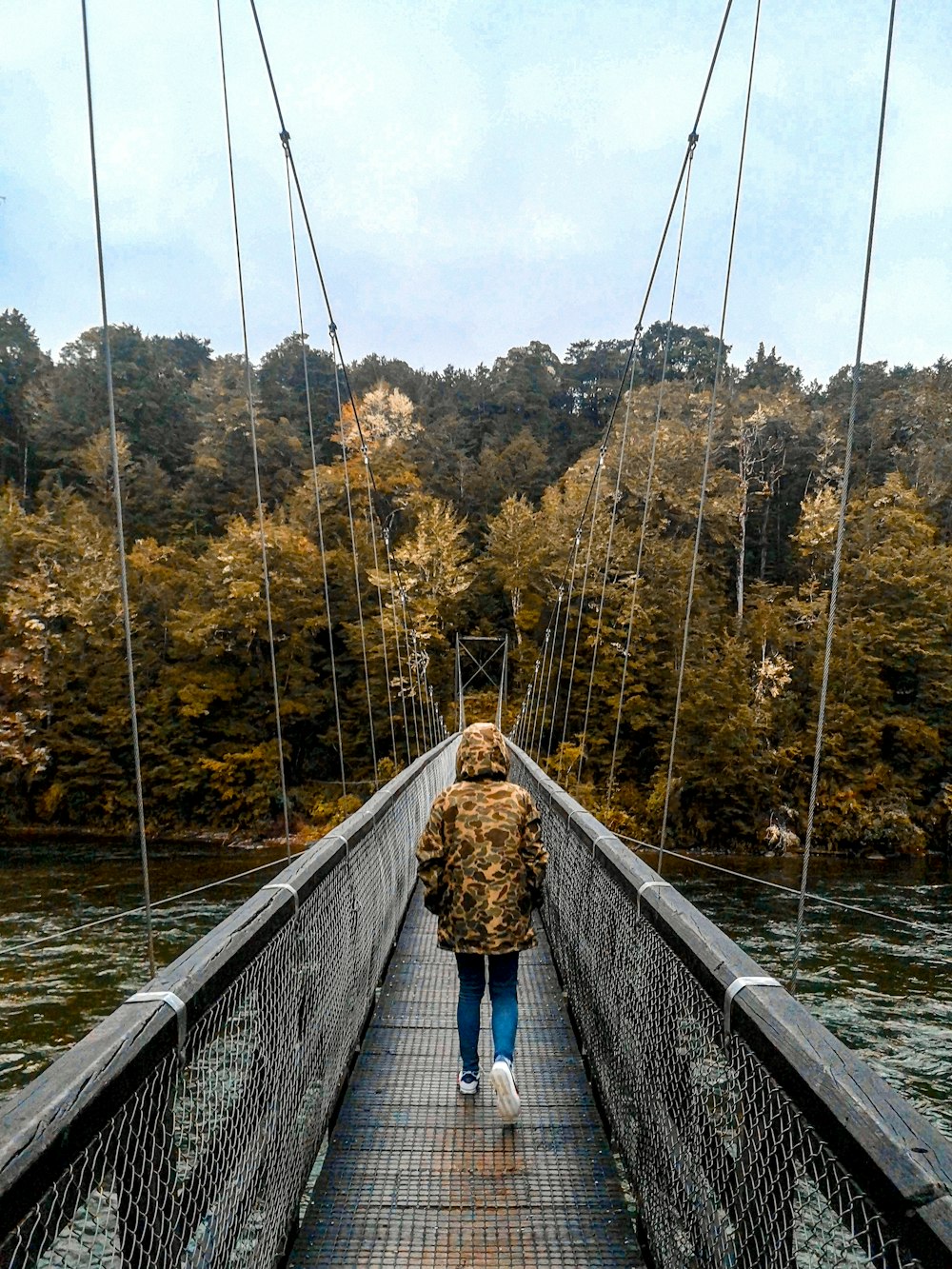 woman in blue shirt and blue denim jeans walking on hanging bridge