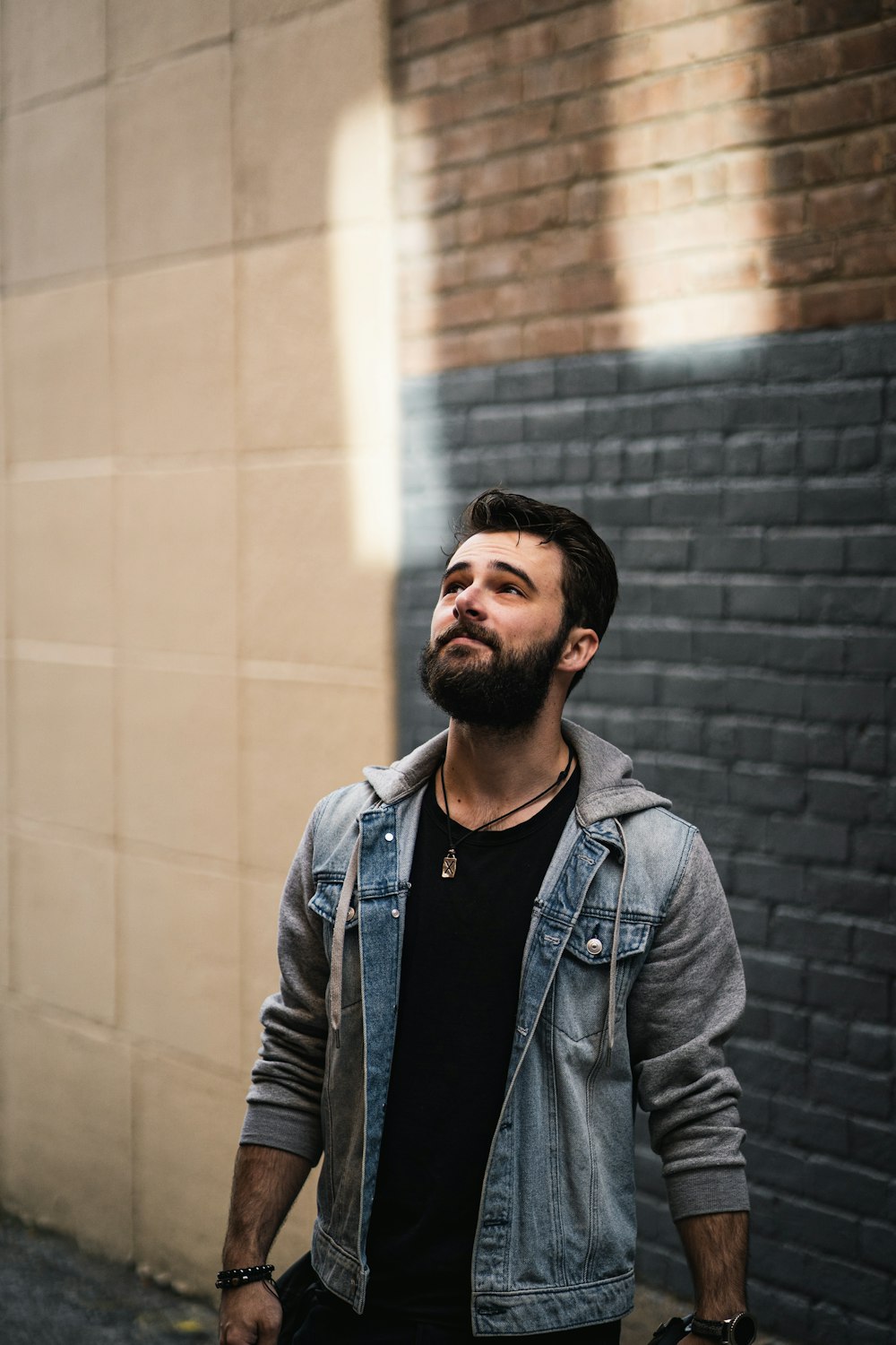 man in black leather jacket standing beside brick wall