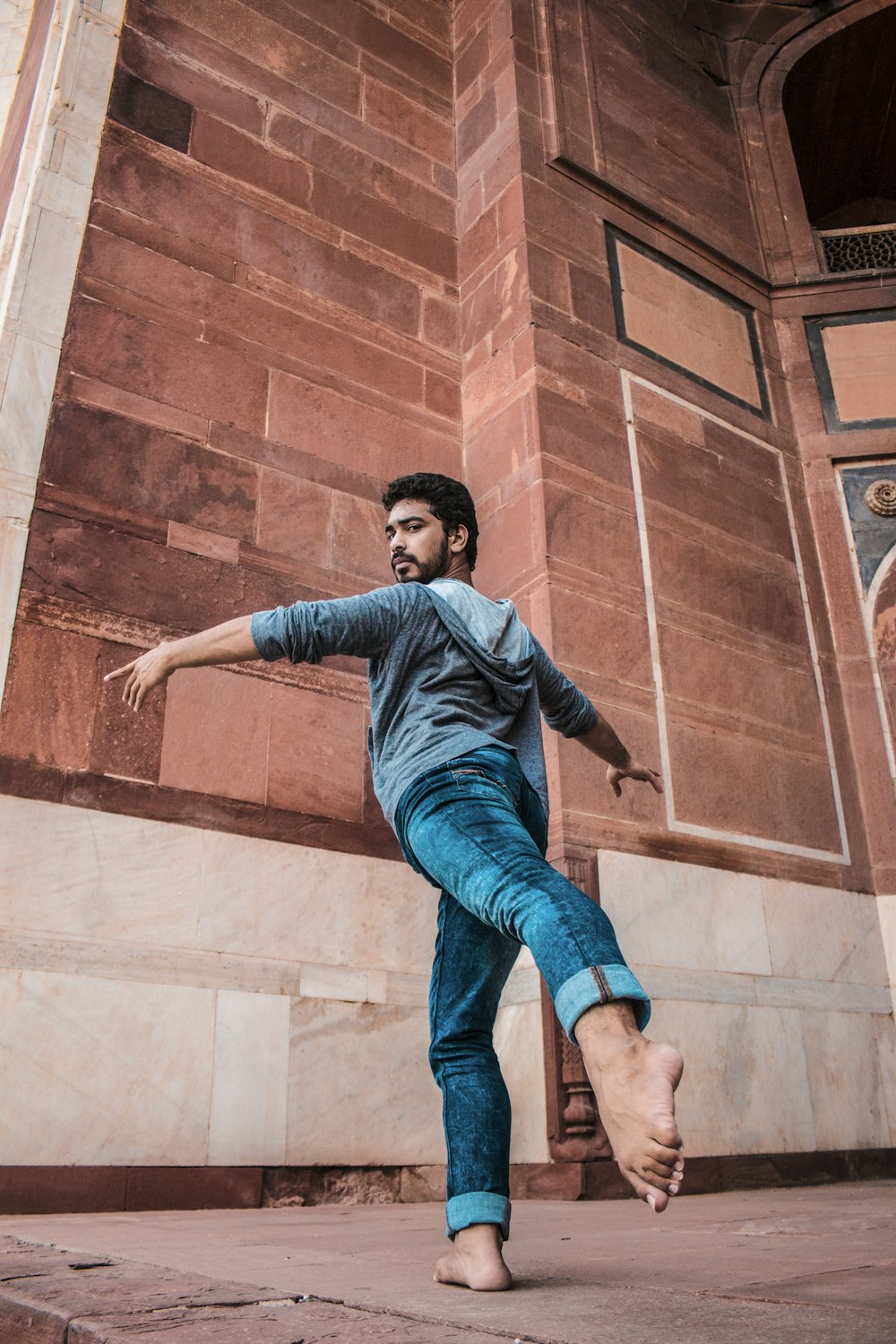 homem em jeans azuis saltando na parede de concreto marrom durante o dia