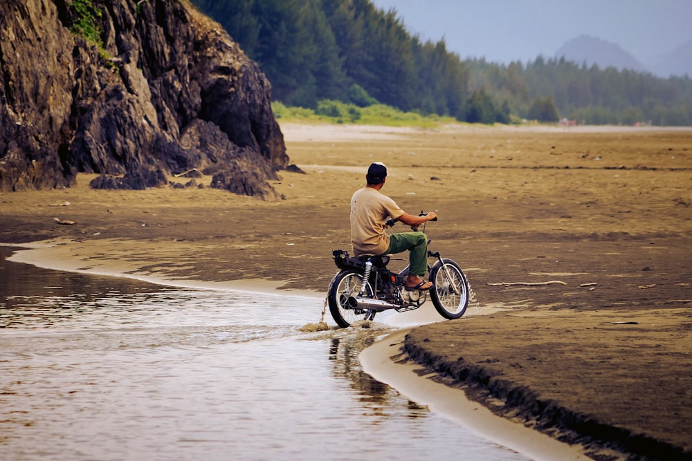 Mann im braunen Hemd fährt tagsüber auf grünem Motorrad auf braunem Sand