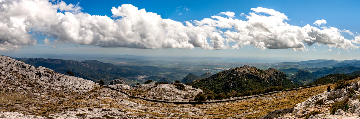 Bare rocky slopes in the Serra de Tramuntana under heavy white clouds, with lowland beyond
