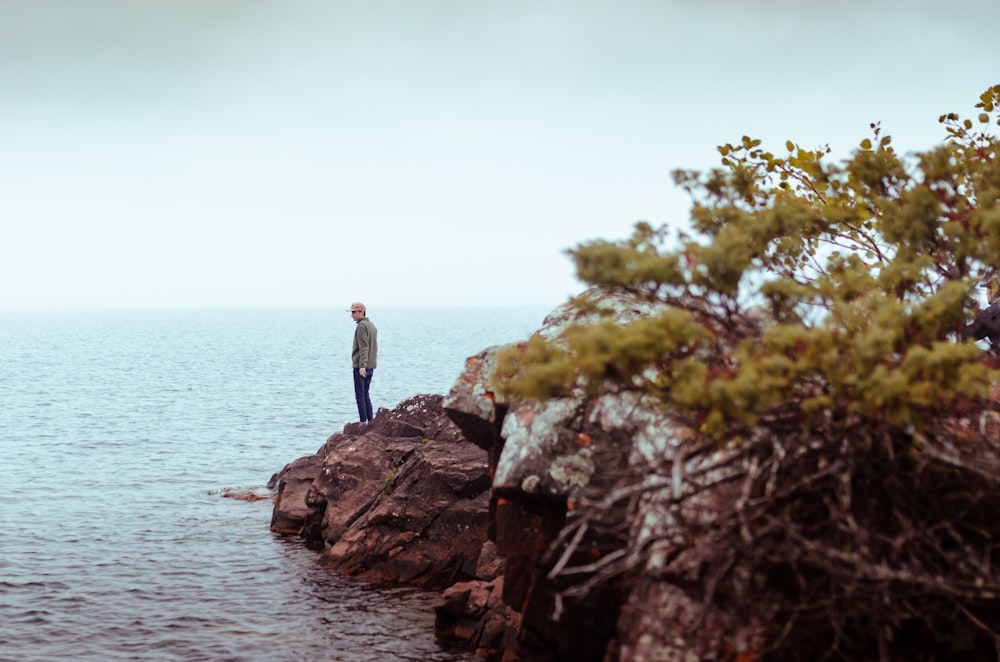 man in black jacket standing on rock near body of water during daytime