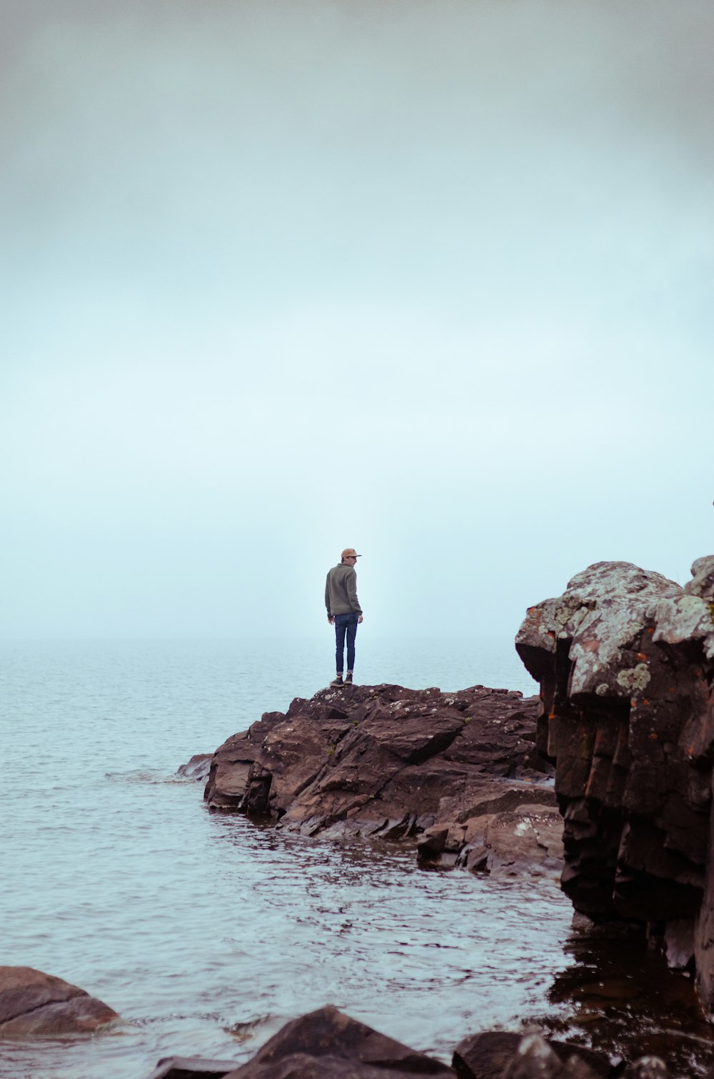 man standing on rock formation near body of water during daytime