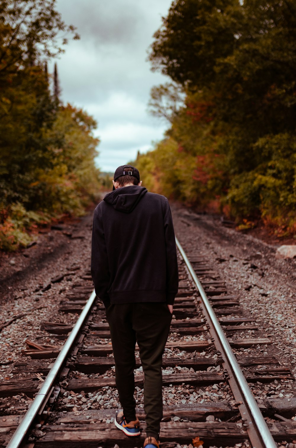 man in black hoodie and brown pants standing on train rail during daytime