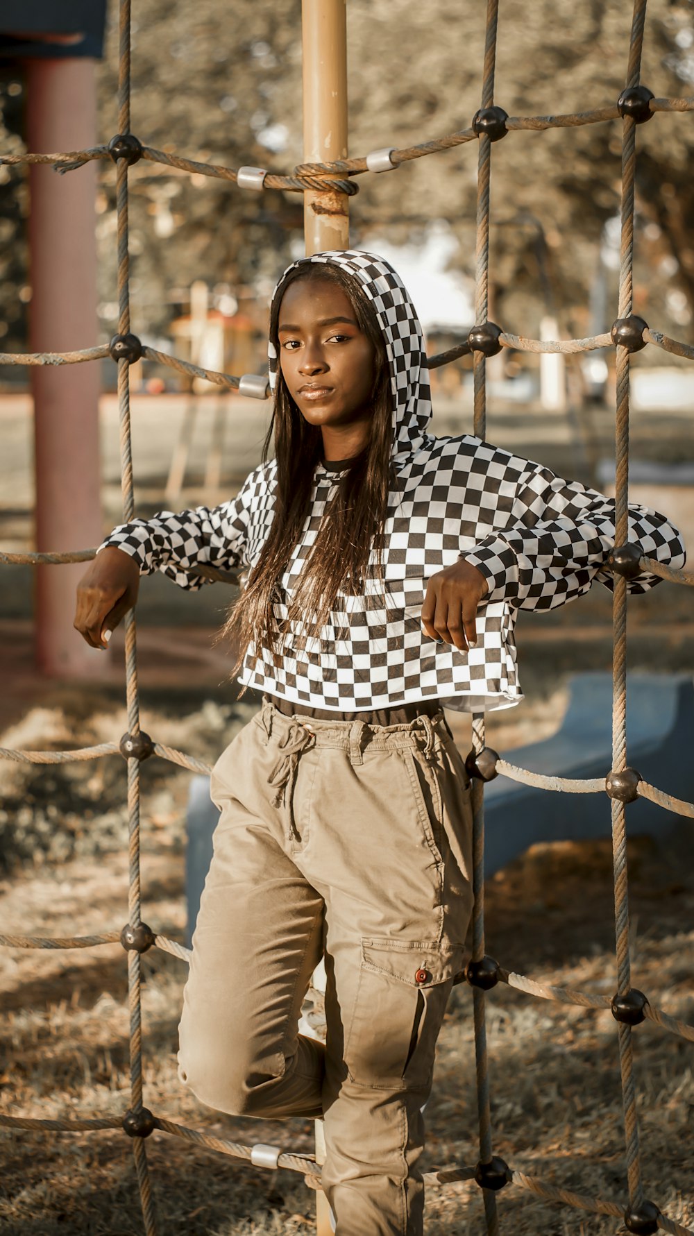 woman in black and white checkered dress shirt and brown pants standing near brown metal fence