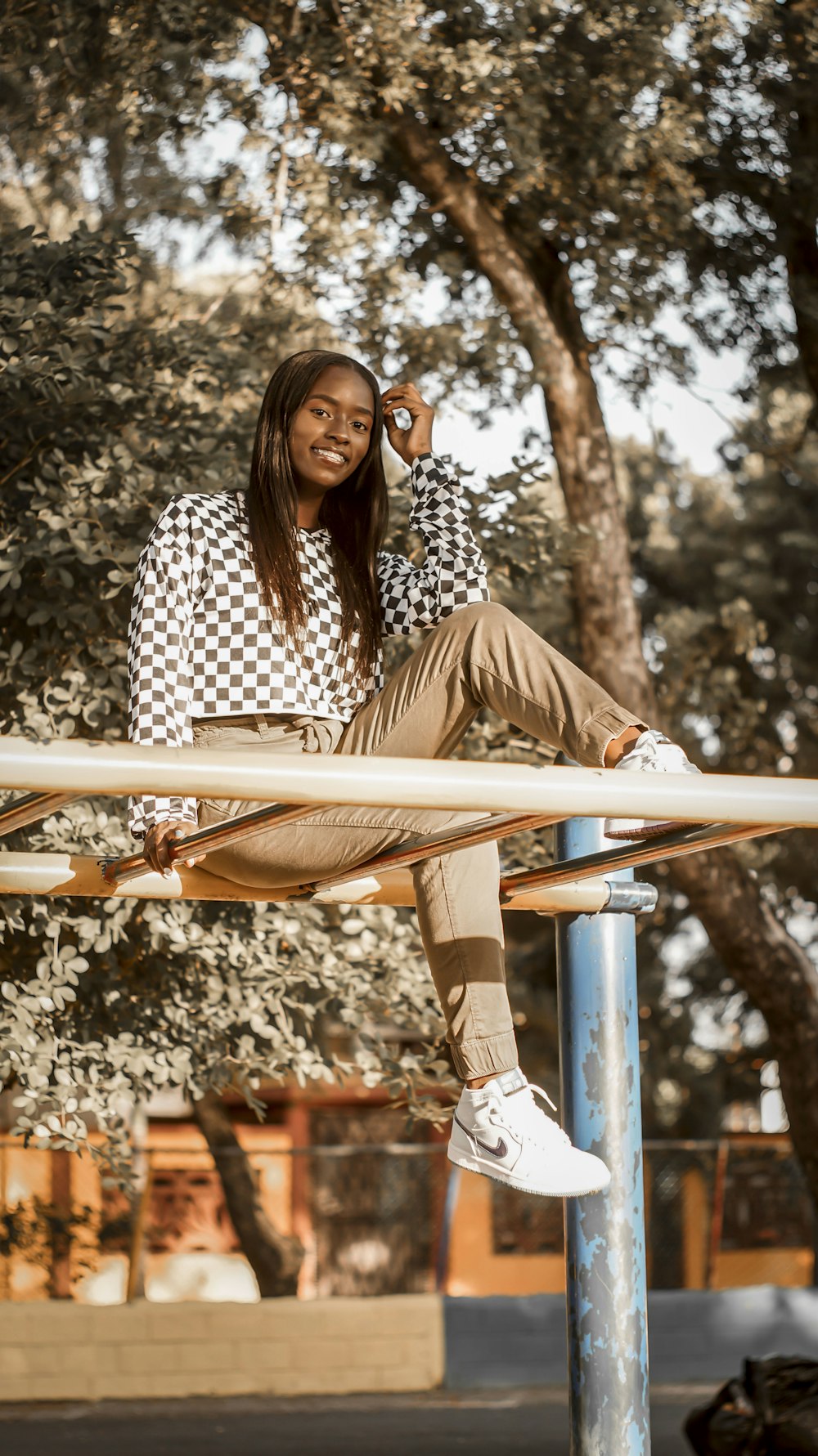 woman in black and white checkered long sleeve shirt sitting on brown wooden ladder during daytime