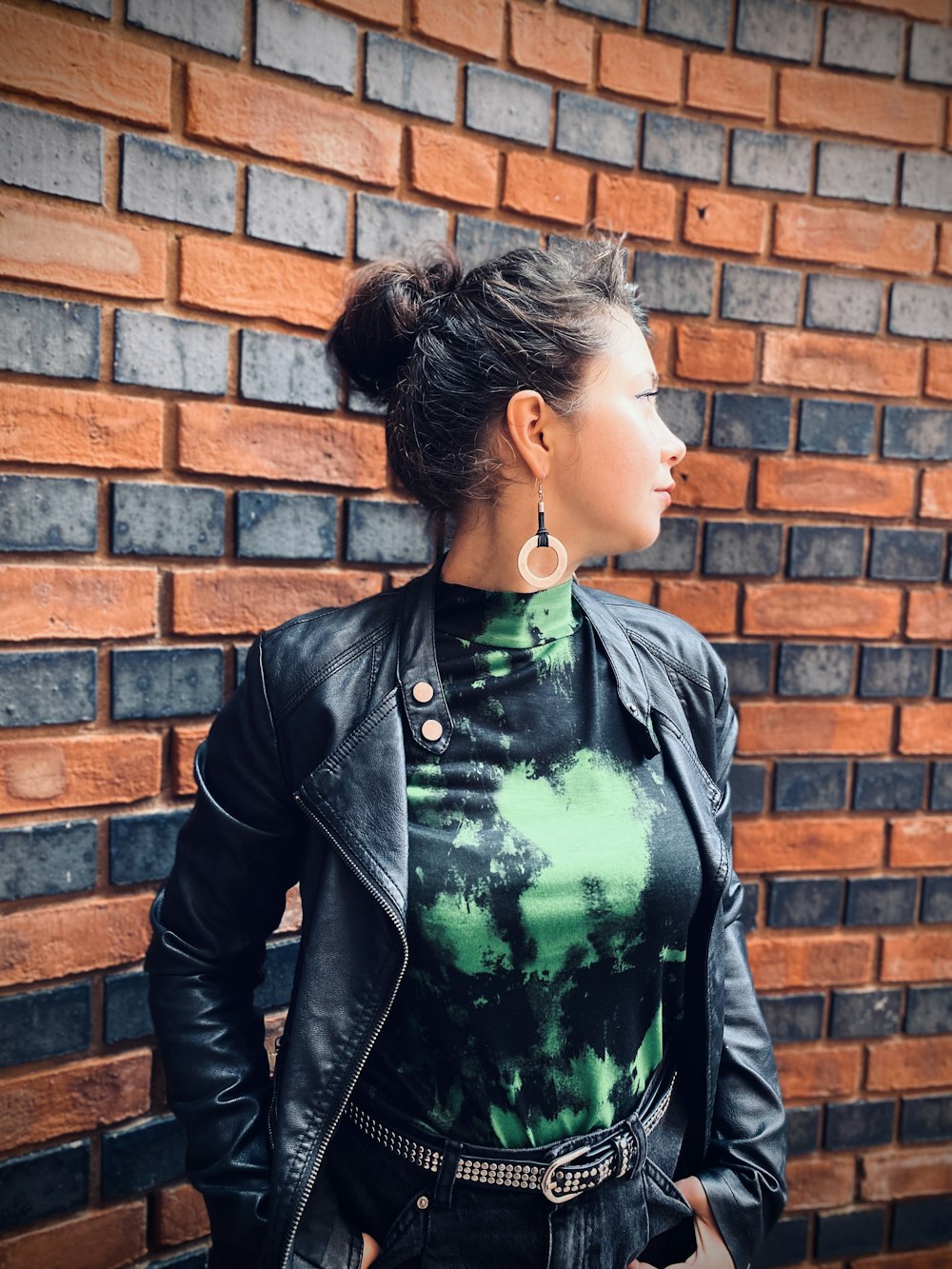 woman in black leather jacket standing beside brown brick wall