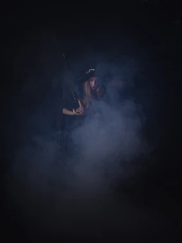 A shadowy figure of The Devil tarot card surrounded by swirling smoke and flickering candlelight.