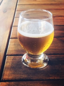 A rustic wooden table displaying a frosty pint of amber ale with bubbles rising.