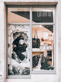 A shop window display featuring artistic decorations with a lunar theme, including a large crescent moon and abstract, cloud-like elements. Inside, there are various bags and framed artworks on display. The overall setting is artistic and visually intriguing, with a mix of modern and whimsical elements.