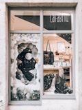 A shop window display featuring artistic decorations with a lunar theme, including a large crescent moon and abstract, cloud-like elements. Inside, there are various bags and framed artworks on display. The overall setting is artistic and visually intriguing, with a mix of modern and whimsical elements.