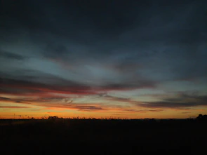 A dramatic silhouette of a rugged outback landscape at sunset, with deep orange and purple hues painting the sky.
