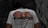 A person is wearing a white t-shirt with a colorful dragon design and the word 'FORTUNE' printed on the back. The shirt also includes text in a foreign language along with motivational phrases such as 'Fate is influenced by strokes of Good Luck as well as Humup Setbacks.' The setting appears to be outdoors with a stone or graffiti-covered wall in the background.