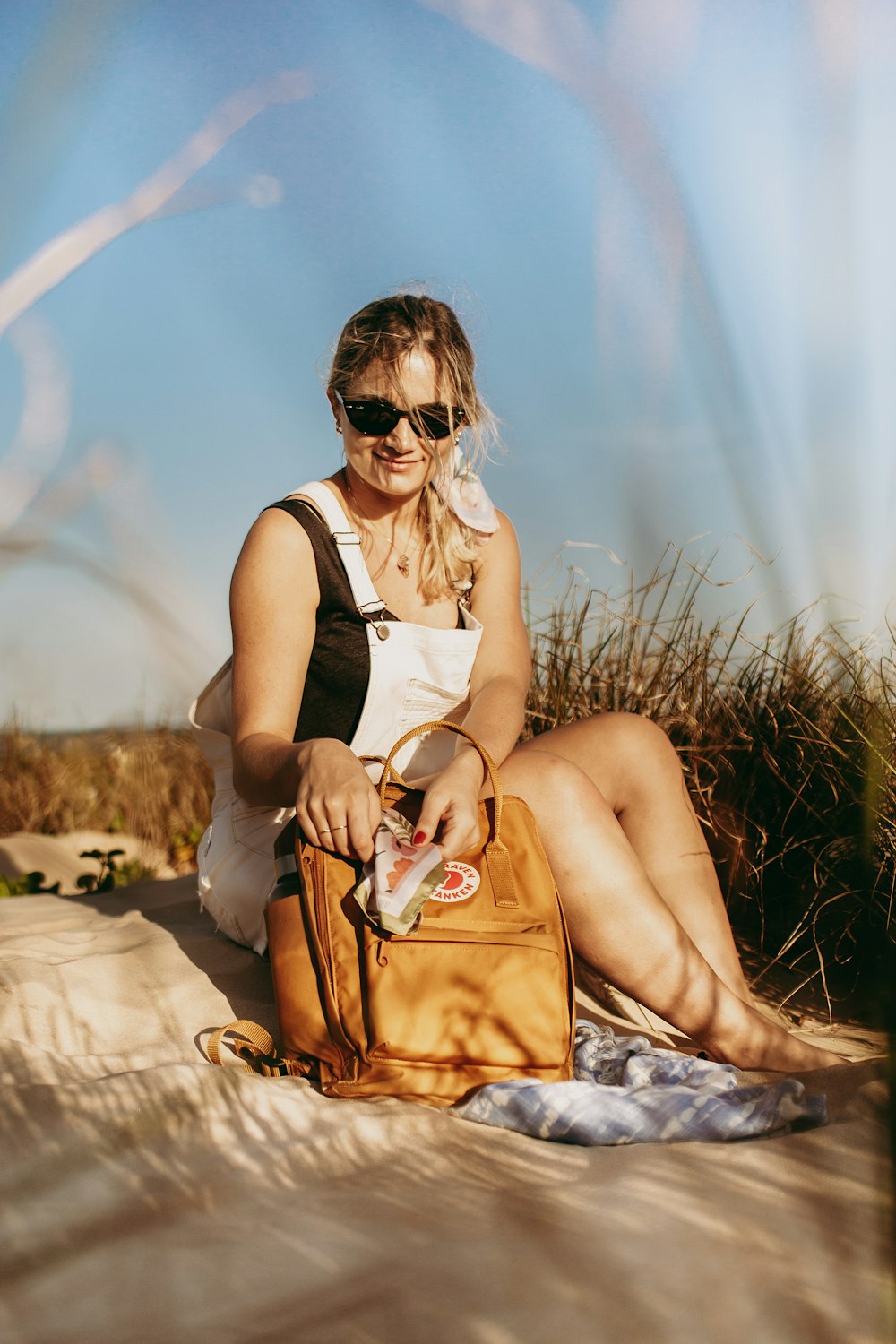 woman in white tank top and brown leather sling bag sitting on brown grass during daytime
