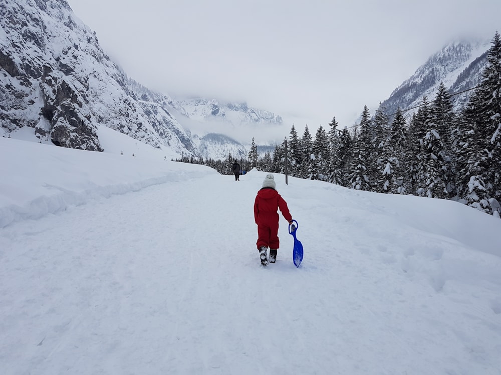 person in red jacket and blue pants walking on snow covered ground during daytime