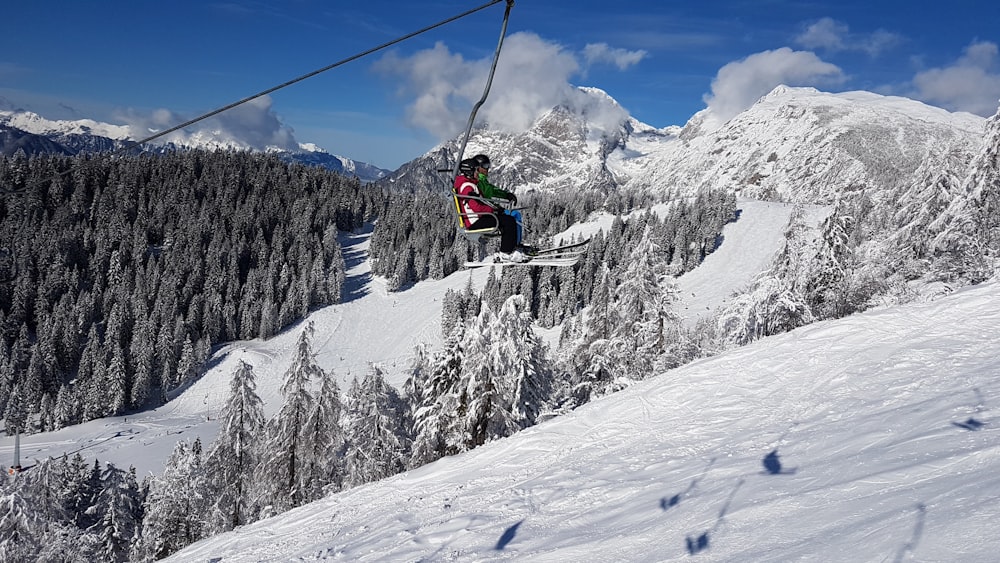 person in red jacket riding ski lift over snow covered mountain during daytime