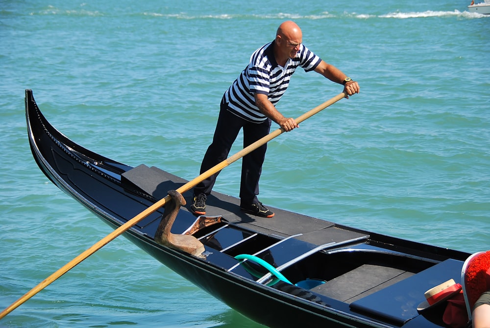 man in blue and white striped long sleeve shirt riding on black boat during daytime