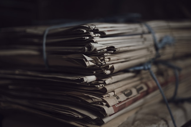 A stack of old newspapers tied together with a blue string, creating a sense of nostalgia and history. The newspapers are yellowed with age, and the lighting is dim, casting soft shadows.